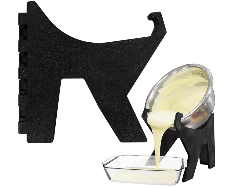 Black plastic tripod support under a mixing bowl with batter that is being poured into a baking dish