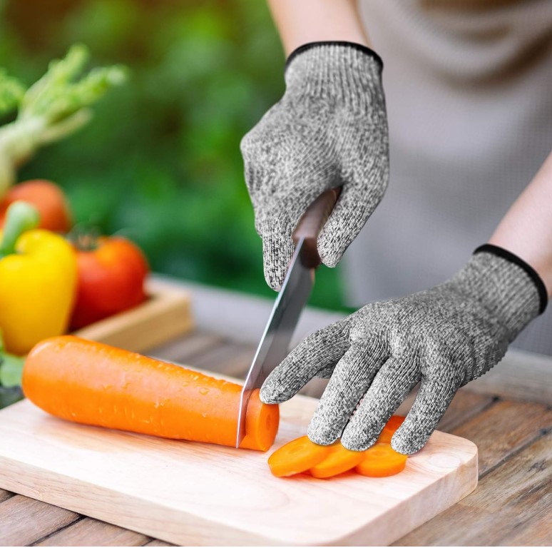 Person wearing gray gloves holding a knife and cutting a carrot on a cutting board