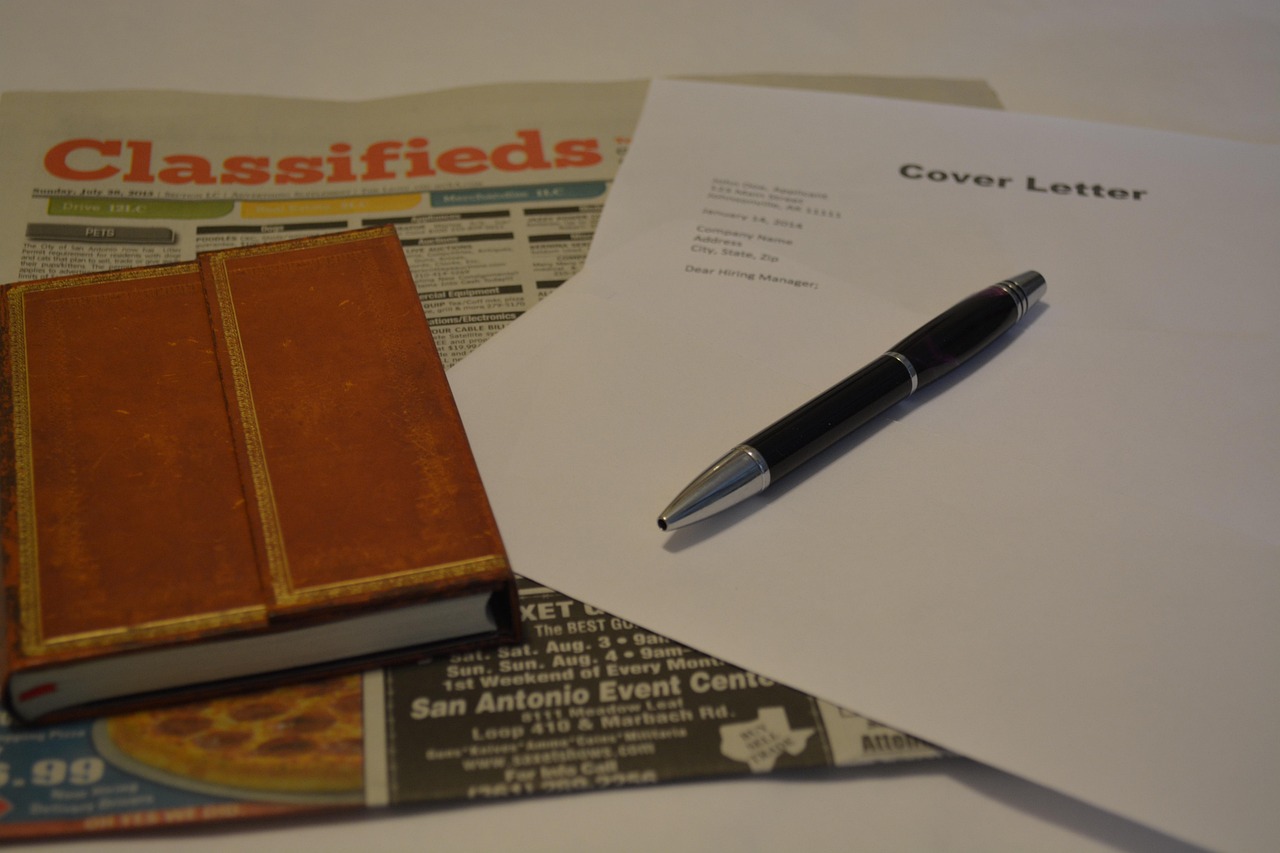 pen, job application, classified section of newspaper and padfolio