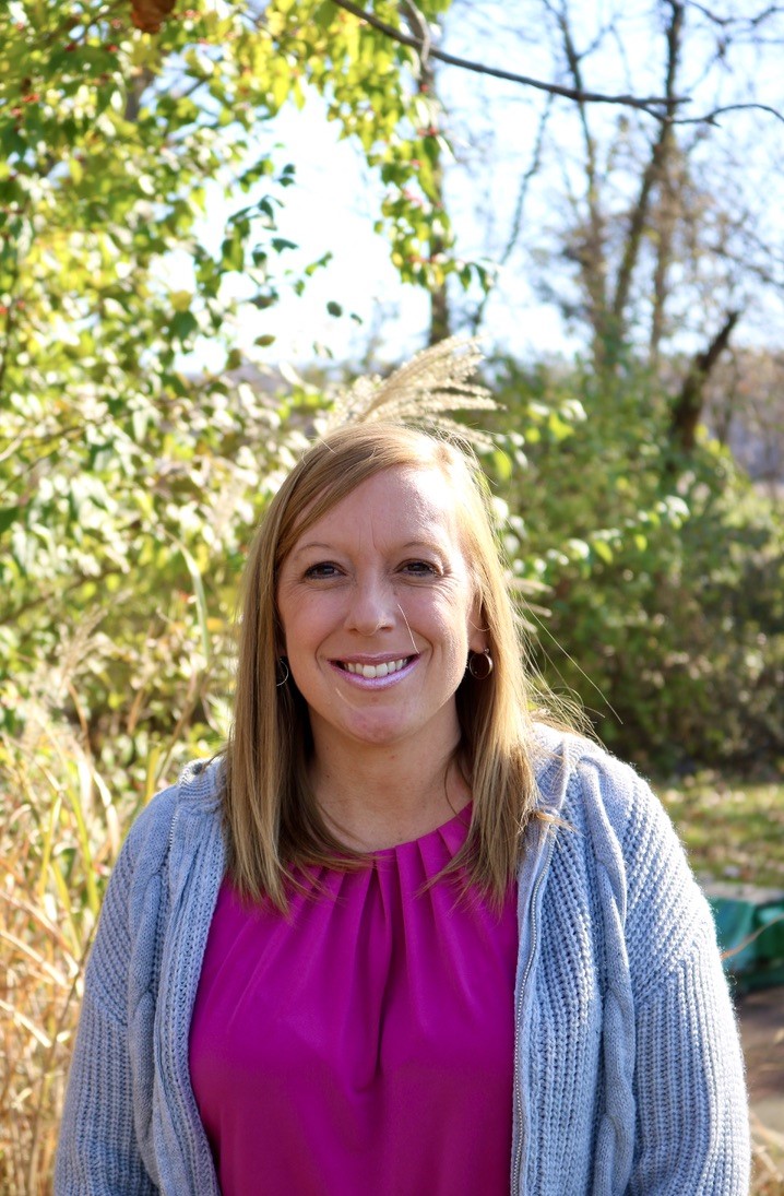 Picture of a woman in pink smiling in front of a green tree