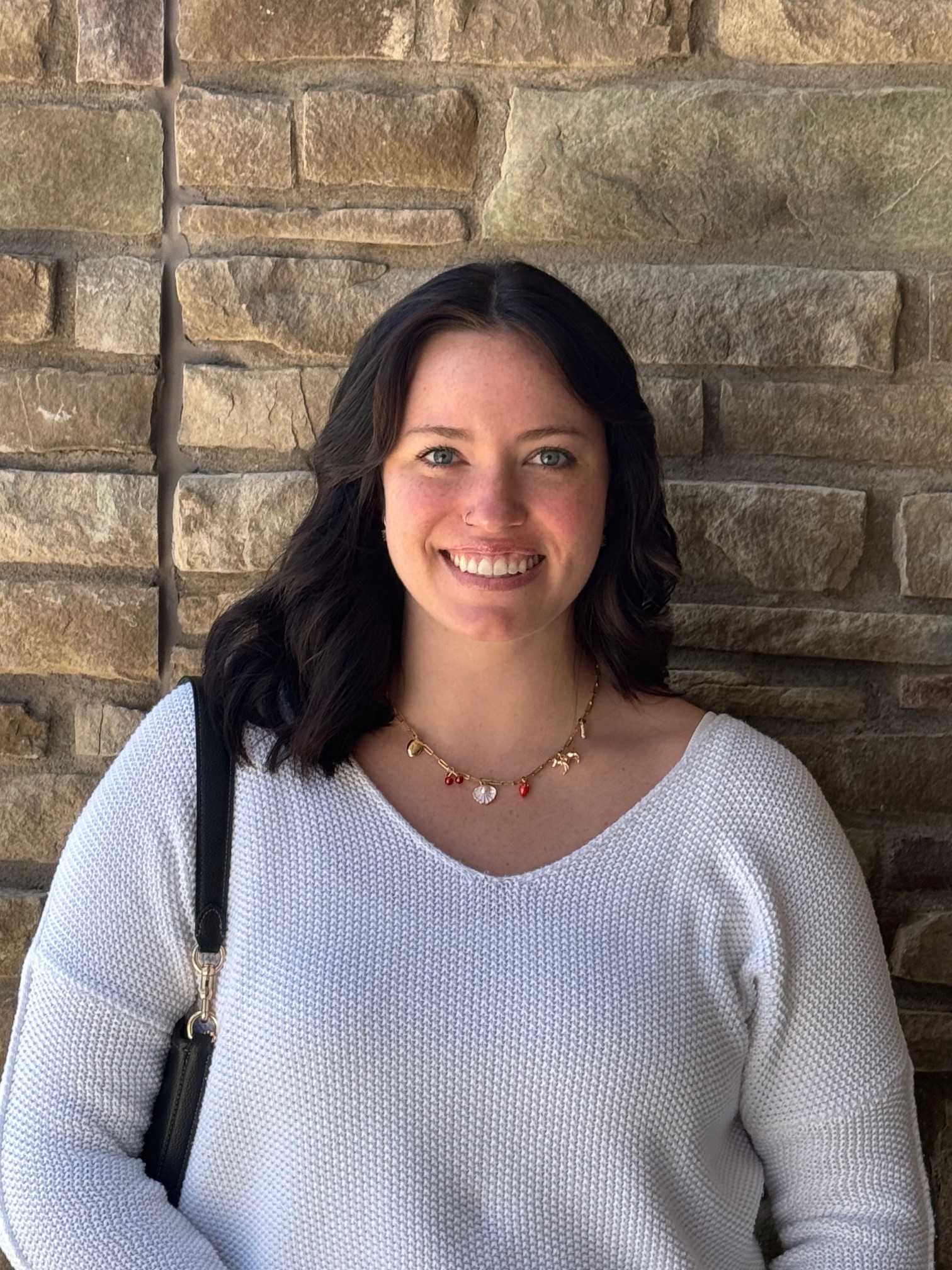 Picture of a woman with dark hair smiling in front of a brick wall