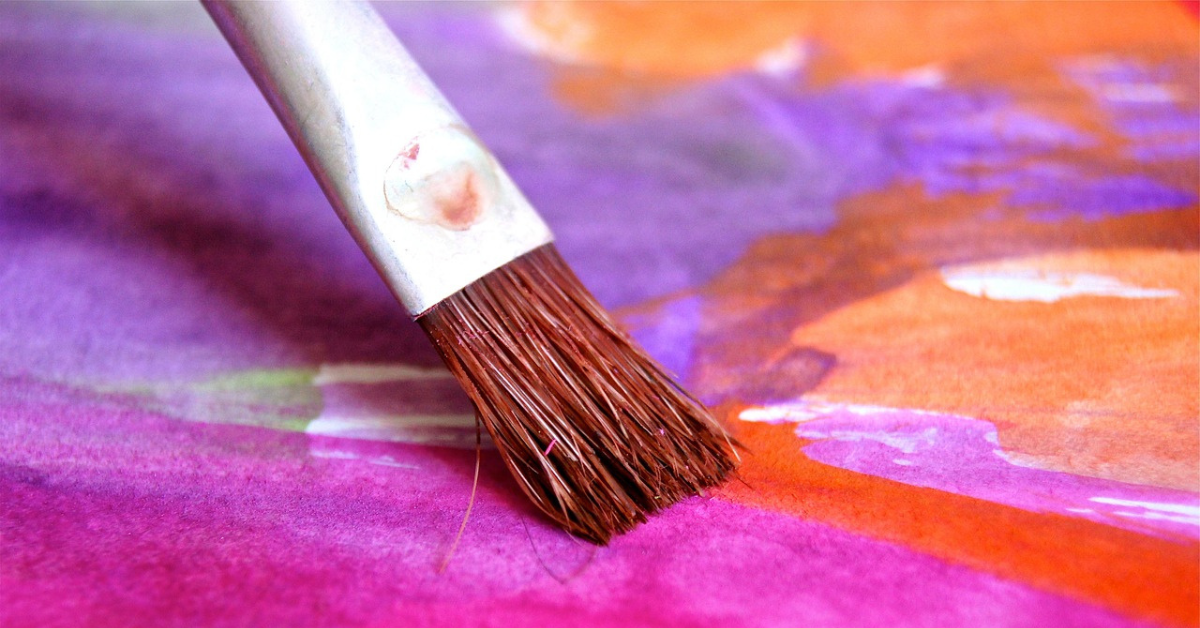 Foto de archivo en la que se ve un pincel pintando en rosa y morado sobre un lienzo.
