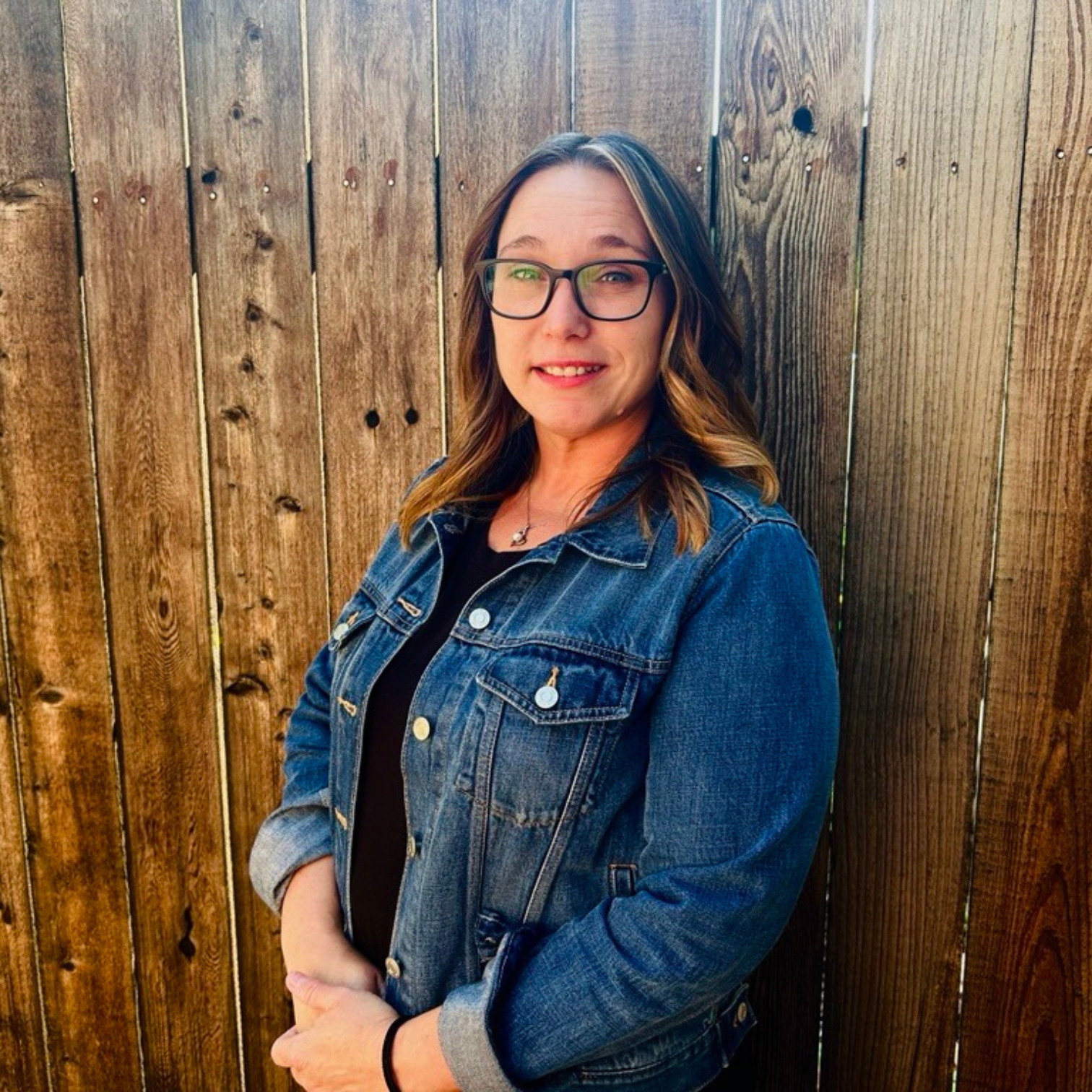 Image of a woman in a jean jacket standing against a wood fence