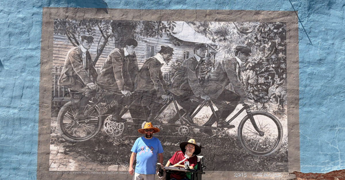 Photo of Michael exploring and posing in front of a mural of five men riding bikes.