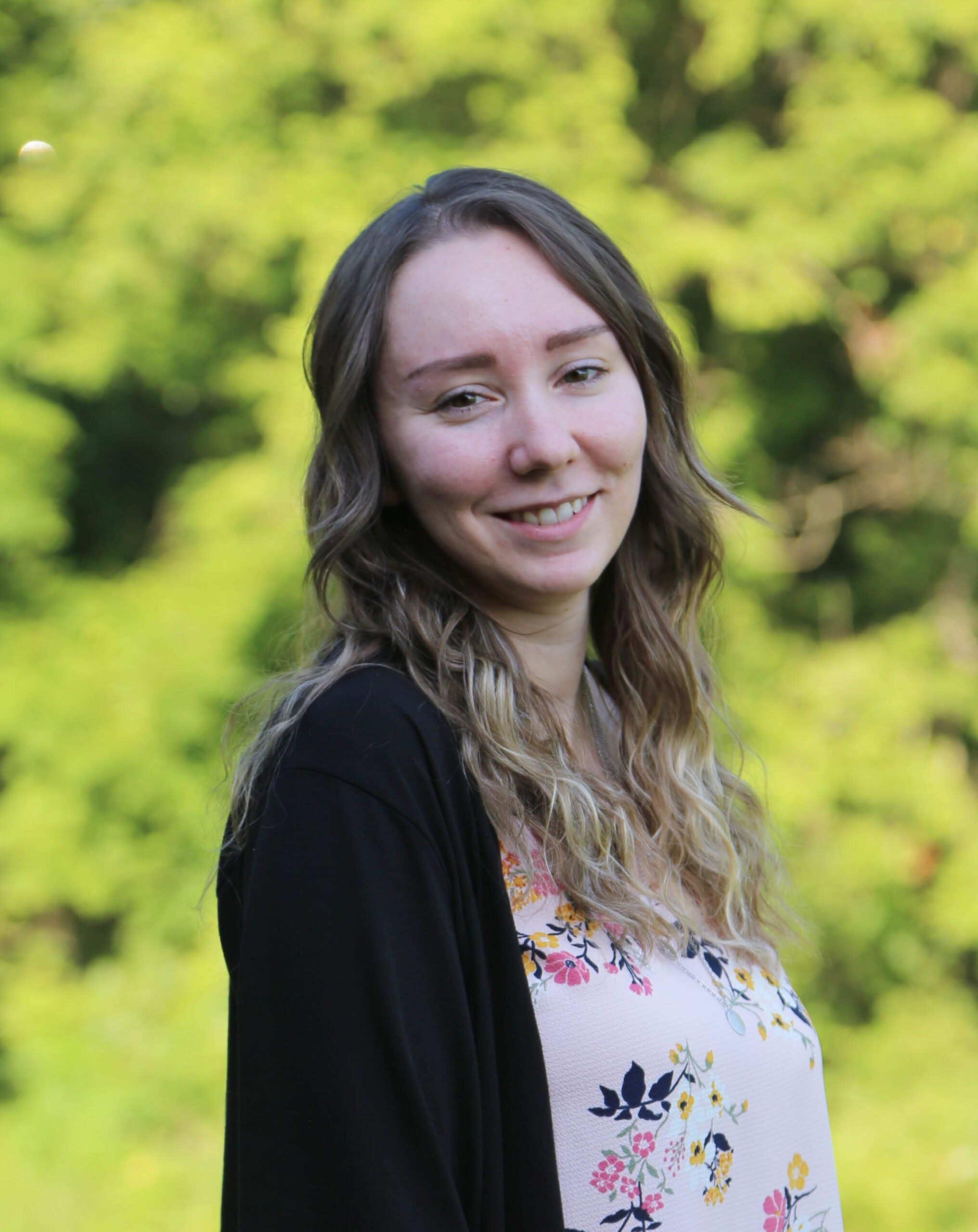woman smiling in front of green trees.